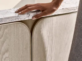 Close-up of a hand resting on a marble countertop above light wood cabinet doors with modern metal handles.