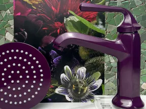 Purple faucet and matching showerhead on a marble surface with floral and mosaic green tile background.