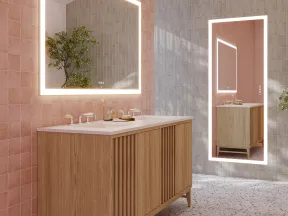 Modern bathroom with wooden vanity, illuminated mirrors, pink and gray tiled walls, terrazzo floor, and green plants.