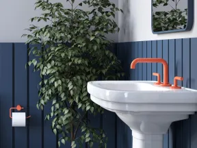 Modern bathroom corner with white pedestal sink, orange faucet, navy paneling, large potted plant, and wall mirror.