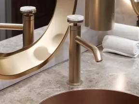 Modern gold faucet and round sink on marble countertop with mirror and rolled white towels in bathroom.