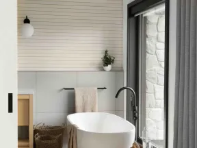 Modern minimalist bathroom with freestanding tub, wooden stool, large window, and neutral decor elements.