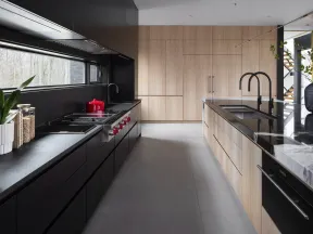 Modern kitchen with black and light wood cabinetry, black countertops, marble island, and large window overlooking trees.