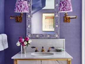 Elegant bathroom vanity with floral patterned mirror, purple walls, gold accents, and decorative lighting.
