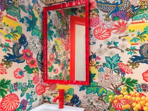 Vibrant bathroom with floral and dragon wallpaper, red framed mirror, red faucet, and patterned decor accents.