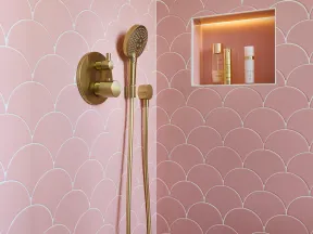 Modern shower with gold fixtures and pink scalloped wall tiles featuring a built-in illuminated niche with toiletries.