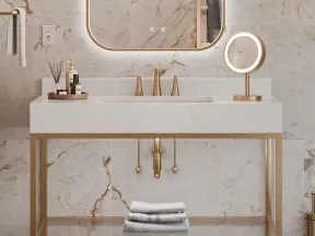 Modern bathroom sink with gold fixtures, illuminated mirror, marble walls, and neatly folded towels on shelf.