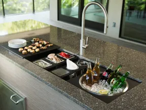 Outdoor kitchen countertop with built-in sink, ice bucket with drinks, appetizers, and modern faucet under natural light.