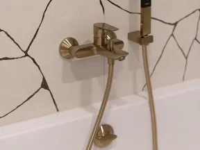 Modern gold bathtub faucet and hand shower against white wall with black abstract lines in a bathroom.