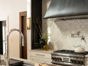 Modern kitchen with stainless steel stove, stylish hood, marble countertop, and freshly sliced bread on cutting board