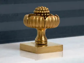 Ornate gold decorative knob with rounded petals and a textured spherical center on square base.