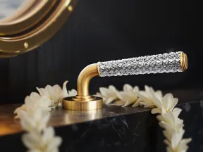 Elegant gold and crystal door handle on black marble surface decorated with white flower garland under a round mirror.
