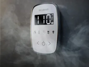Digital steam shower control panel showing 110°F with visible steam around it on a dark tiled wall