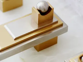 Modern abstract sculpture with gold and silver geometric shapes and a metallic sphere on a white surface.
