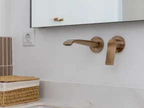 Modern bathroom sink with wall-mounted brushed brass faucet and woven storage basket on marble countertop.