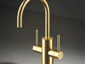 Modern matte gold kitchen faucet with dual handles on gray stone countertop and dark background.