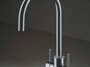 Modern stainless steel kitchen faucet with dual handles and a high curved spout on a gray surface.