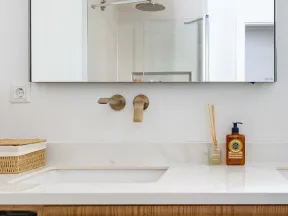 Modern bathroom sink with brushed brass faucet, large mirror, wooden vanity, and toiletry accessories on countertop