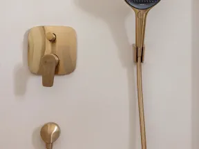 Modern gold showerhead and matching control knobs mounted on a clean white bathroom wall.