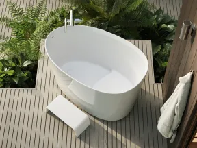 Modern white freestanding bathtub on wooden deck surrounded by green plants with towel hanging nearby