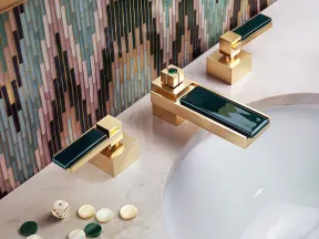 Gold and dark green faucet on marble sink with colorful geometric tile backsplash and game pieces scattered on countertop.