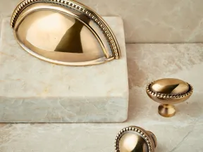 Antique brass cabinet handles and knobs with decorative beaded edges on marble surface.