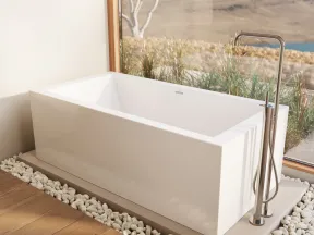 Modern white freestanding bathtub with stainless steel faucet by large window overlooking landscape.
