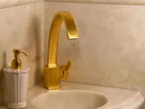Modern bathroom sink with a curved beige marble countertop and matte gold faucet and soap dispenser.
