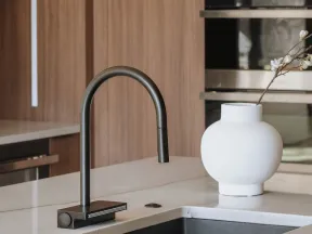 Modern kitchen sink with black faucet and white vase on marble countertop in a wood-paneled kitchen.
