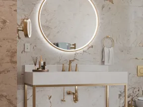 Modern bathroom with a round illuminated mirror, marble walls, gold fixtures, and a minimalist vanity with towels.