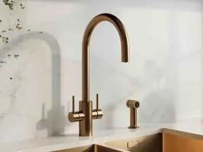 Modern kitchen sink with brushed bronze faucet and dual compartments set in marble countertop.
