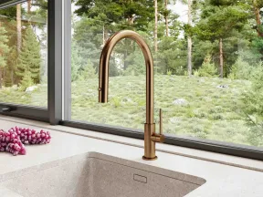 Modern kitchen sink with bronze faucet overlooking a lush green forest through a large window