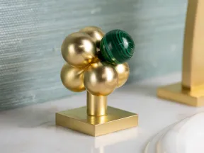 Decorative gold and green spherical cluster sculpture on a marble bathroom countertop near sink.