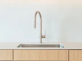 Minimalist kitchen sink with stainless steel faucet, light wood cabinets, and decorative bowls on shelf above.