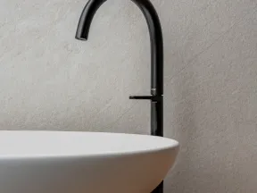 Modern black faucet with a round white ceramic sink on wooden countertop against textured light wall.