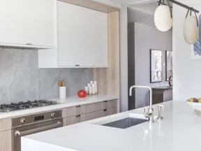 Modern kitchen with white island, stainless steel sink and stove, light wood cabinetry, and contemporary lighting.