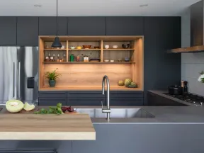 Modern kitchen with grey cabinetry, wooden shelves, stainless steel appliances, and a central island with sink and cutting board.