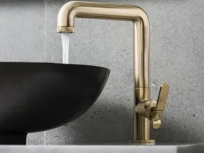 Modern brass faucet with water flowing into a black round vessel sink on a marble countertop.