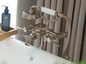 Chrome vintage-style bathtub faucet with handheld shower head mounted on white tub in modern bathroom.