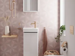 Modern bathroom with geometric pink wall tiles, white floating sink, toilet, and natural decor accents.