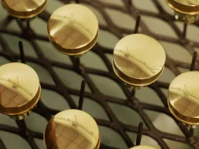 Close-up of shiny gold circular knobs arranged on a metal grid surface with reflections visible on each knob.