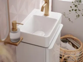 Modern white bathroom sink with gold faucet, soap dispenser, and wicker basket near window and pink wall.