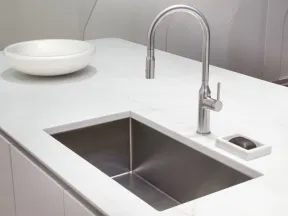 Modern kitchen sink with stainless steel faucet and white marble countertop featuring a soap dish and bowl.