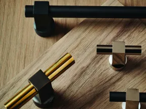 Modern metallic cabinet handles and knobs in black, gold, and chrome finishes displayed on wooden surface.