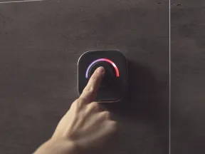 Hand adjusting a modern thermostat dial with blue and red temperature indicators on a dark tiled wall.