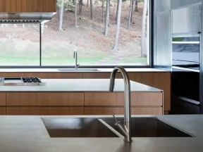 Modern kitchen with stainless steel double sink, wooden cabinets, large window showing wooded outdoor scenery.