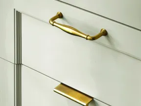Close-up of white cabinetry with two different styles of gold drawer handles.