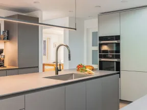 Modern kitchen with gray cabinetry, built-in ovens, a large island with sink, and fresh vegetables on countertop.