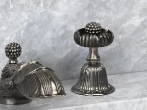 Ornate silver decorative objects with ribbed and fruit-inspired designs on a marble surface.