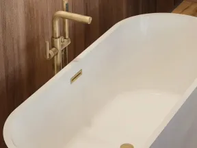 White freestanding bathtub with modern gold faucet against wooden wall in a bathroom.